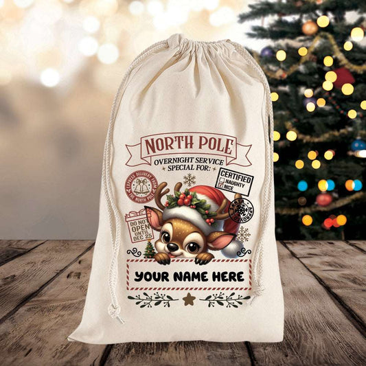 White drawstring bag with reindeer design and text on a wooden surface with a Christmas tree in the background.